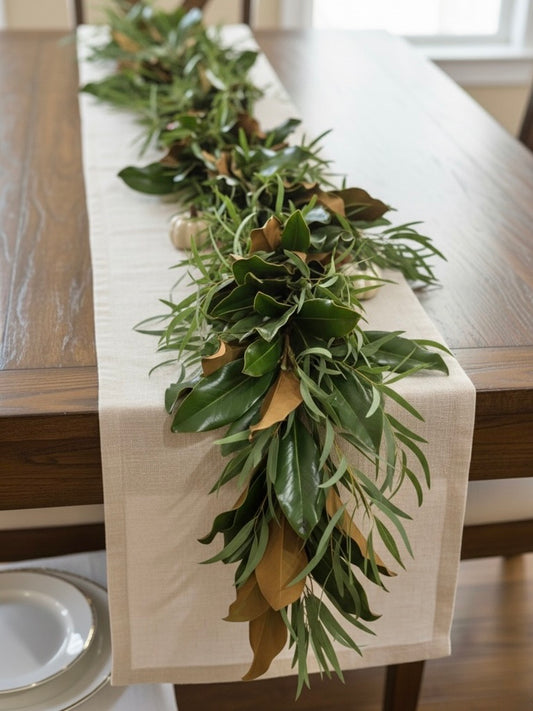 MAGNOLIA Green leafy garland on a white tablecloth over a wooden table.